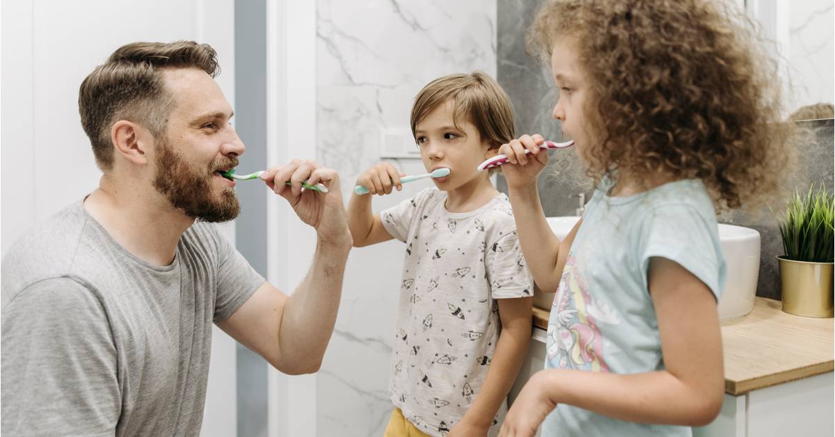 Adult-and-two-kids-brushing-teeth-together-in-a-bathroom