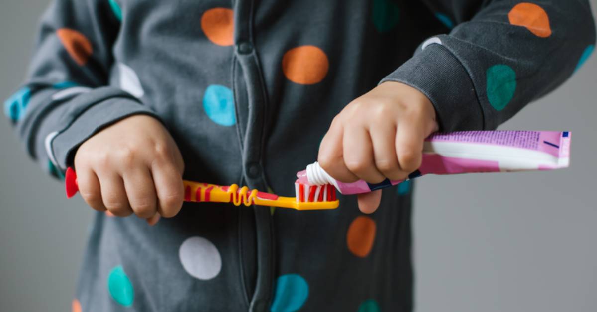 Child-in-polka-dot-pajamas-squeezing-toothpaste-onto-a-toothbrush
