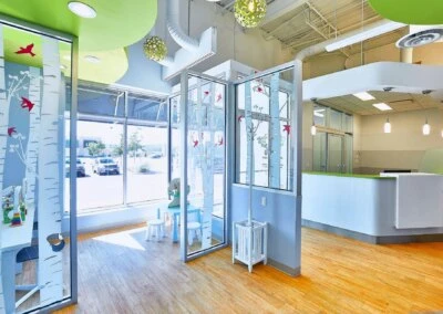 A brightly lit dental clinic reception area and kids' waiting room with colorful decor and birch tree motifs.