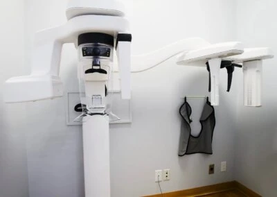 A close-up of a white dental Panorex machine for panoramic X-rays, with a protective vest hanging nearby