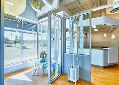 A well-lit waiting area with large windows, a children's play table, and a modern reception desk in the background.